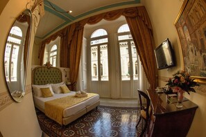 A hotel room with a large bed, a desk, and a chair. There are curtains on the windows and a painting on the wall. - B&B Art Suite Santa Brigida (Naples)
