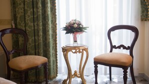 Two wooden chairs with cushioned seats, a small round table with a vase of flowers, and green patterned curtains. - B&B Art Suite Santa Brigida (Naples)
