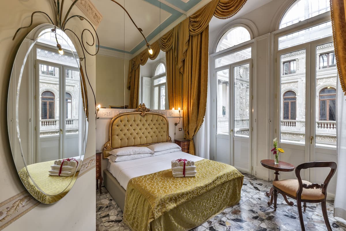 A hotel room with a large bed, a sitting area with a chair, a small table, and a large mirror.