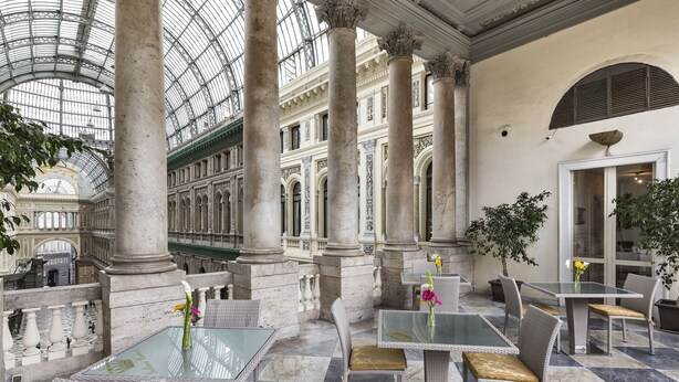 A spacious indoor area with marble flooring and classical columns, featuring tables and chairs for dining. - B&B Art Suite Santa Brigida (Naples)