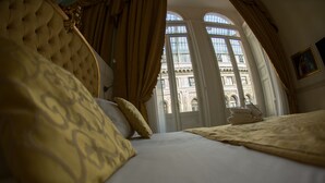 A bed with a tufted headboard, a window with curtains, and a view of a building with arched windows. - B&B Art Suite Santa Brigida (Naples)