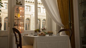 A dining area with a table set for breakfast, a window with curtains, and a view of a building with arched windows. - B&B Art Suite Santa Brigida (Naples)