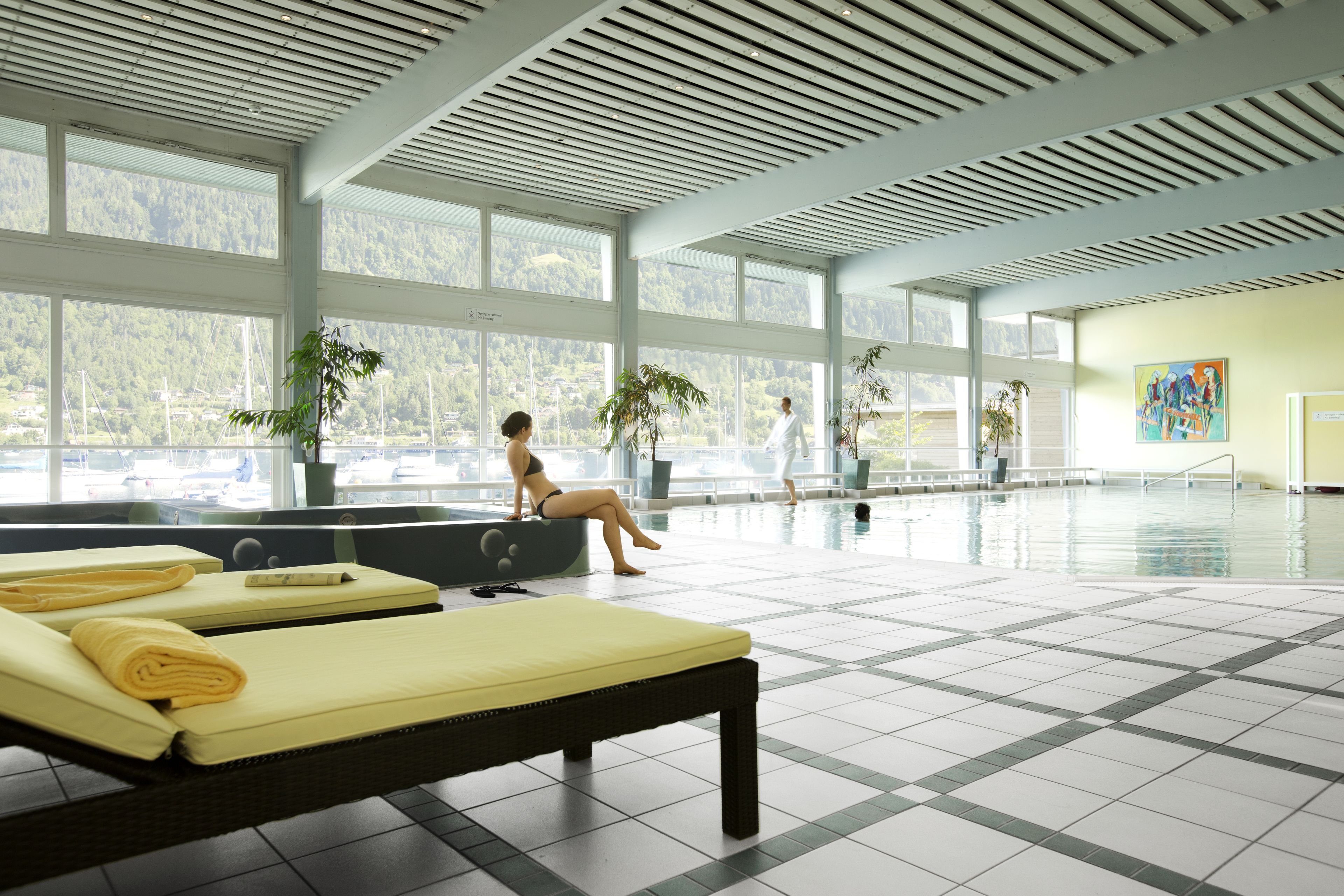 Una amplia piscina interior con grandes ventanales, sillones de descanso y plantas en macetas.