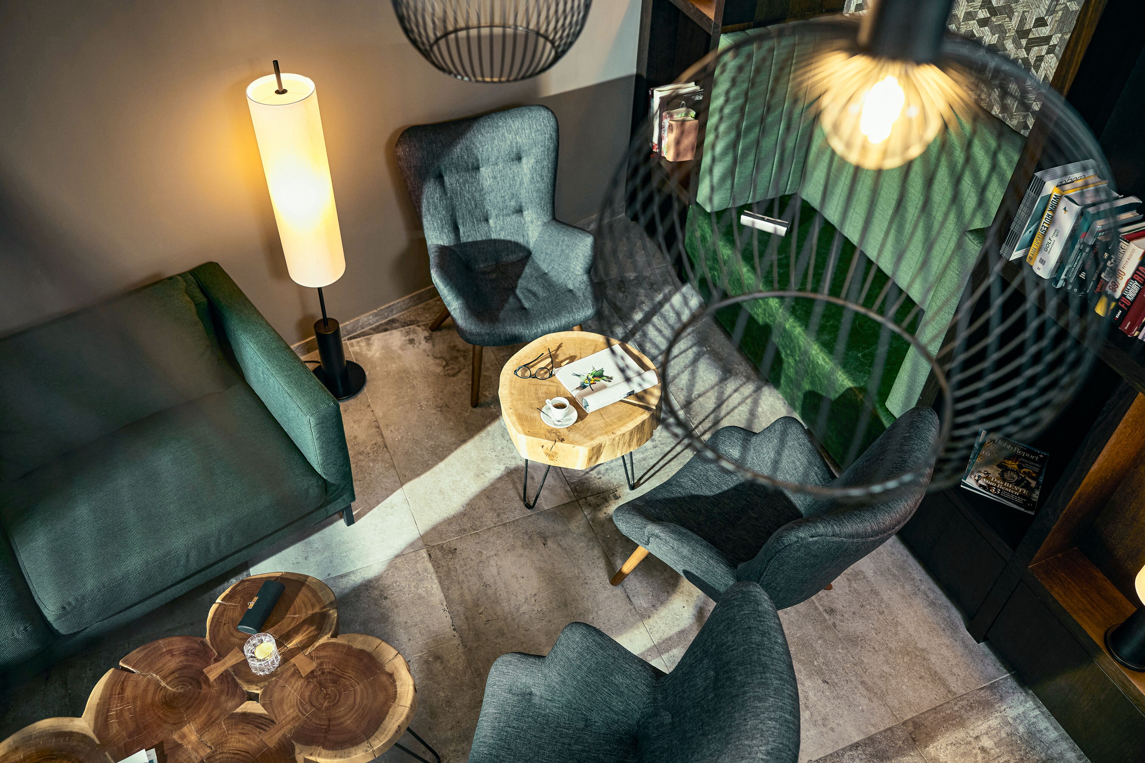 Un espacio lounge moderno con un sofá verde, una mesa de centro redonda de madera y una silla colgante.