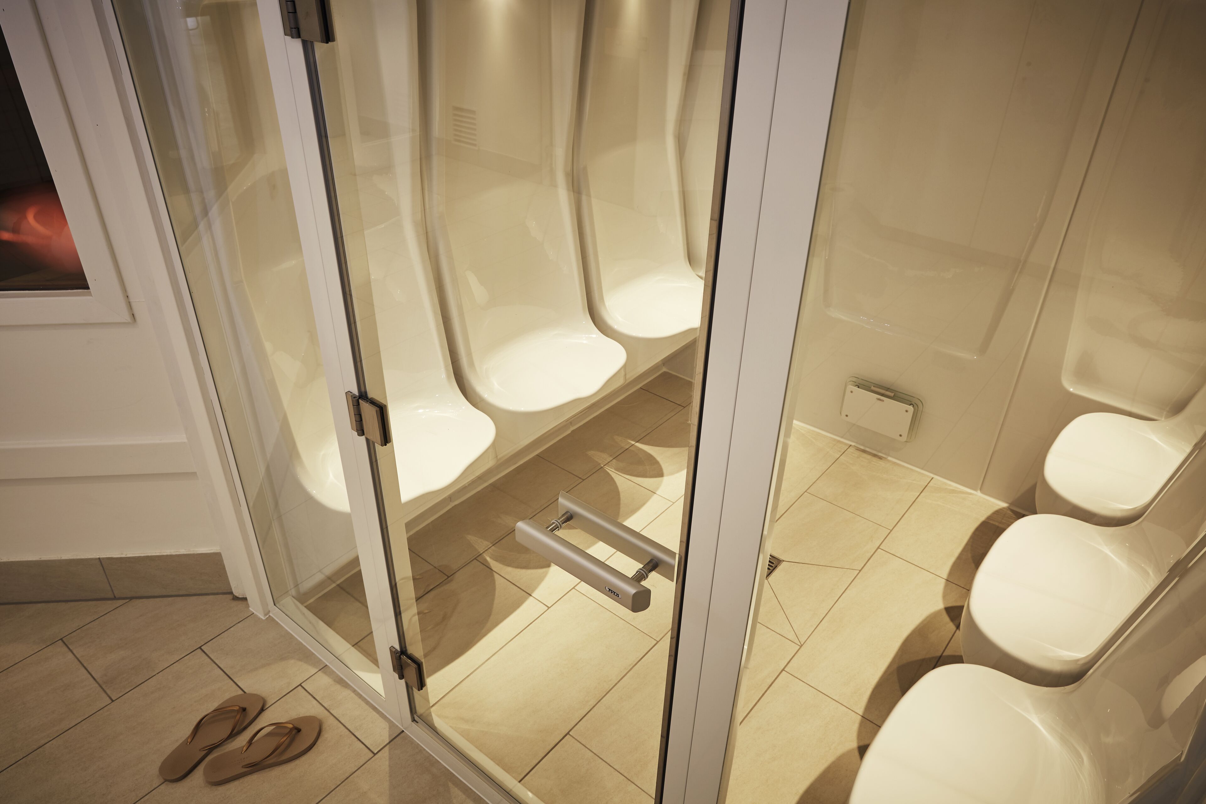 A modern bathroom with a glass partition, three toilets, and a shower area.