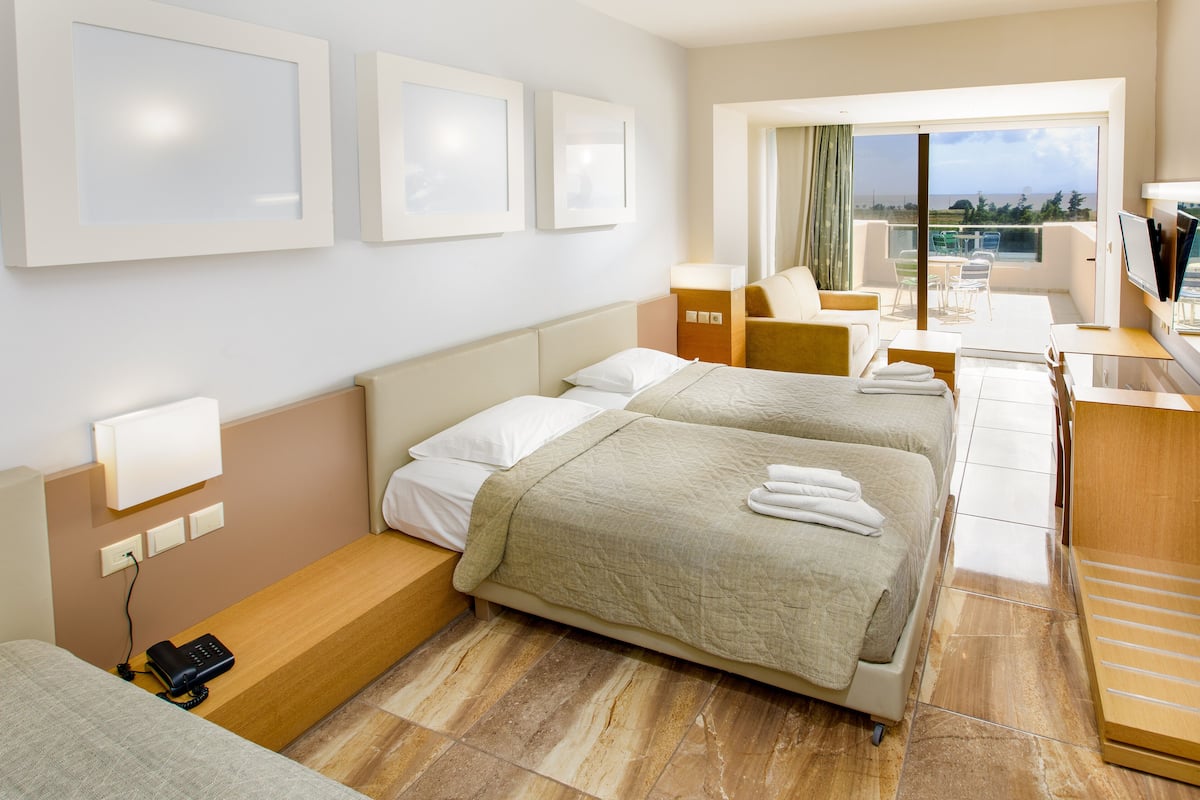 A hotel room with two beds, a desk, a TV, and a balcony with a view.