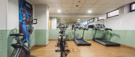 Un gimnasio con bicicletas estáticas, cintas de correr y un espejo grande.
