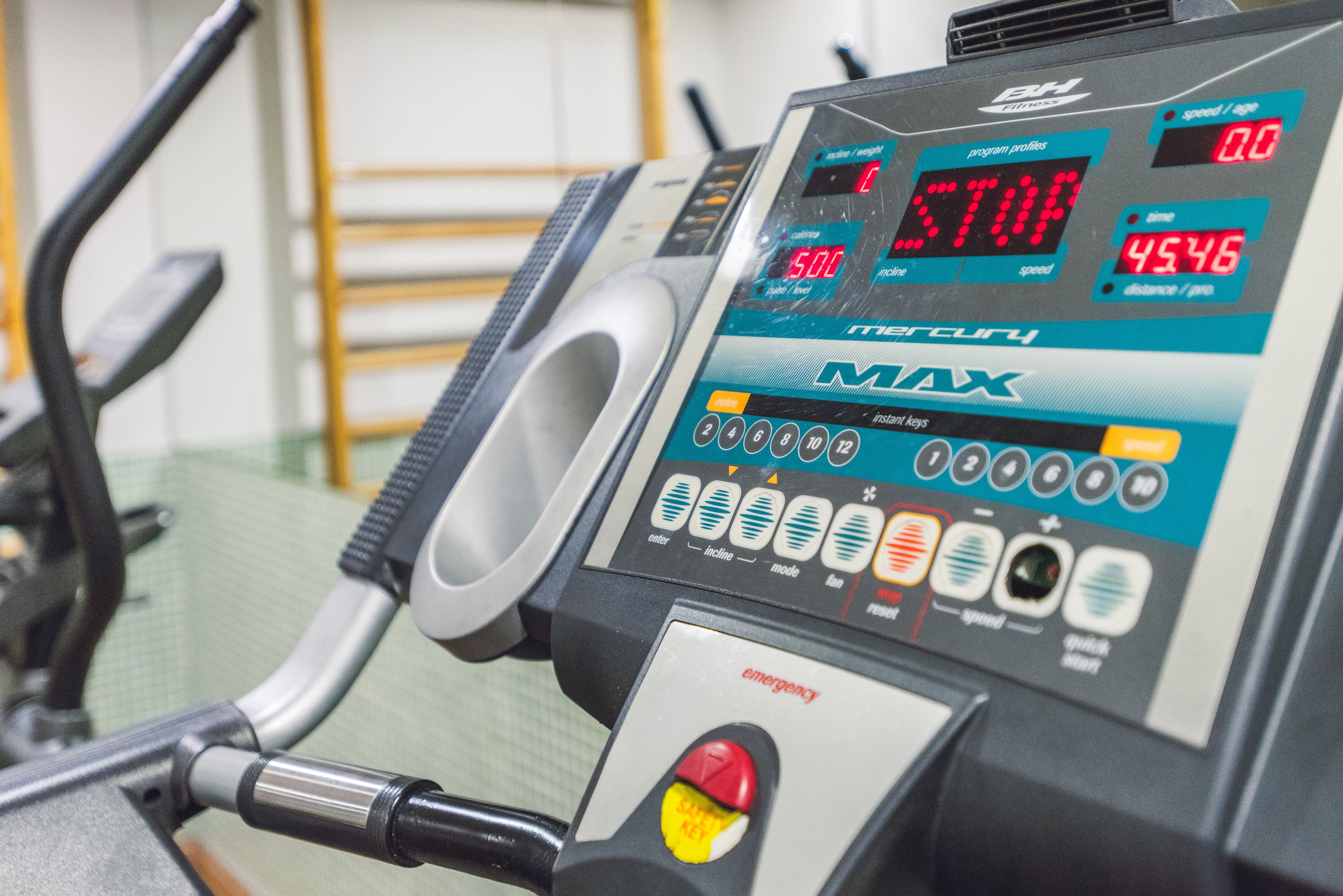 A stationary exercise bike with a digital display, control buttons, and an emergency stop button.