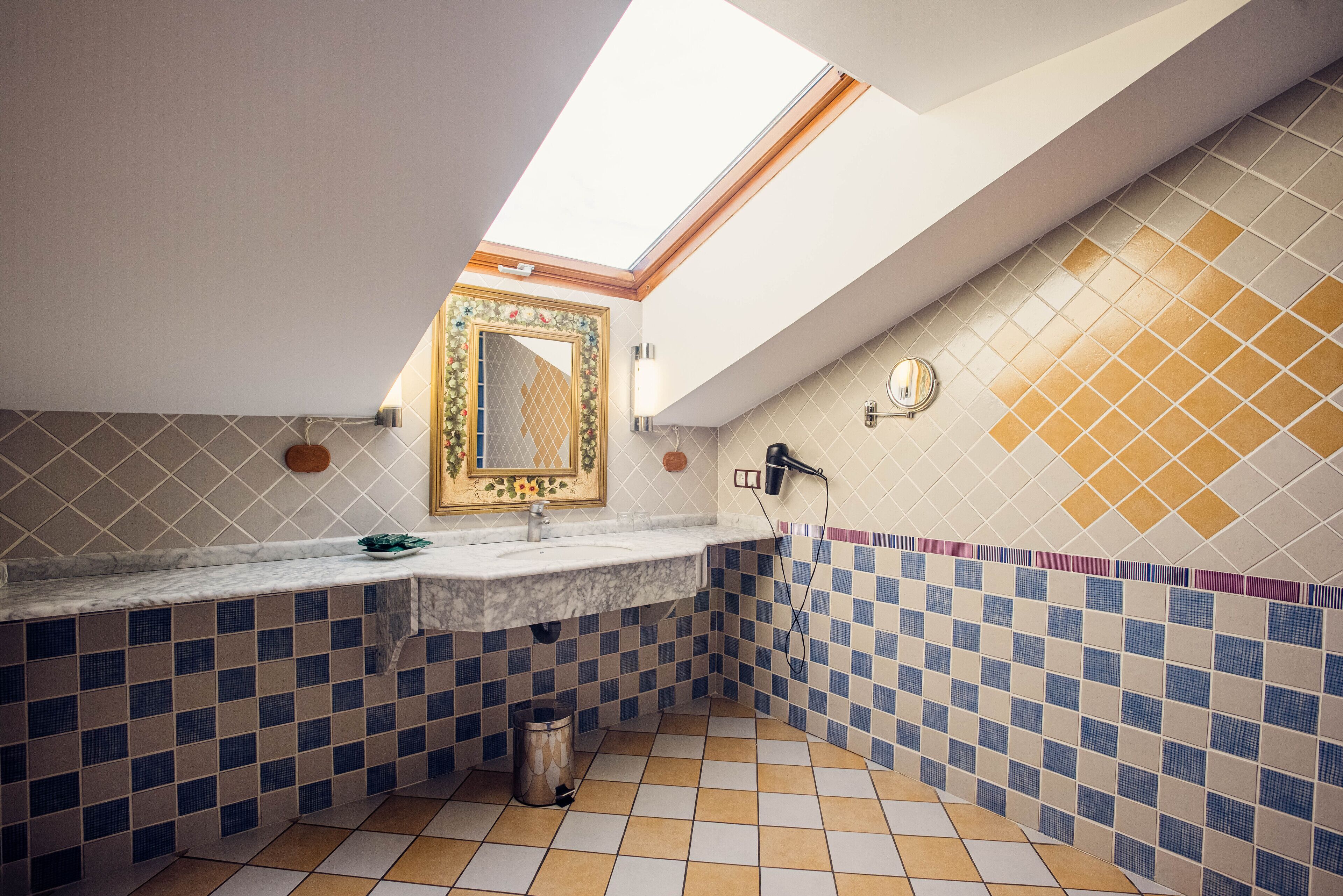 A bathroom with a skylight, a marble sink, a decorative mirror, and checkered tiles.