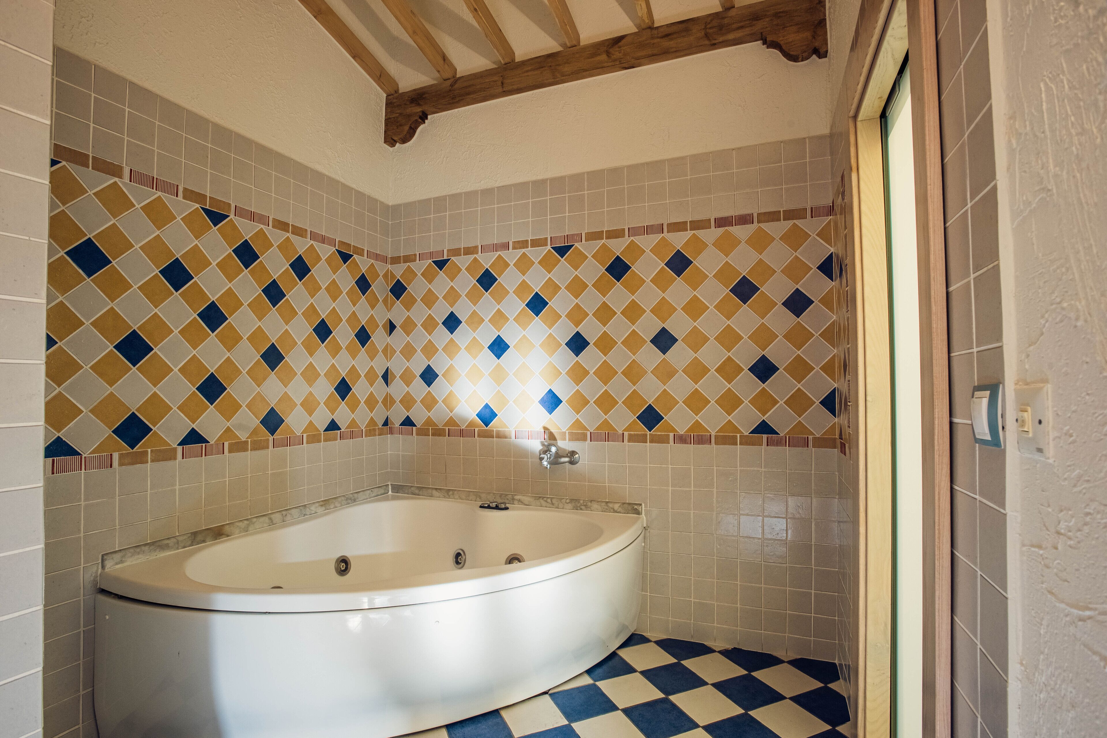 Un baño con bañera independiente, paredes con azulejos y piso de baldosas a cuadros.