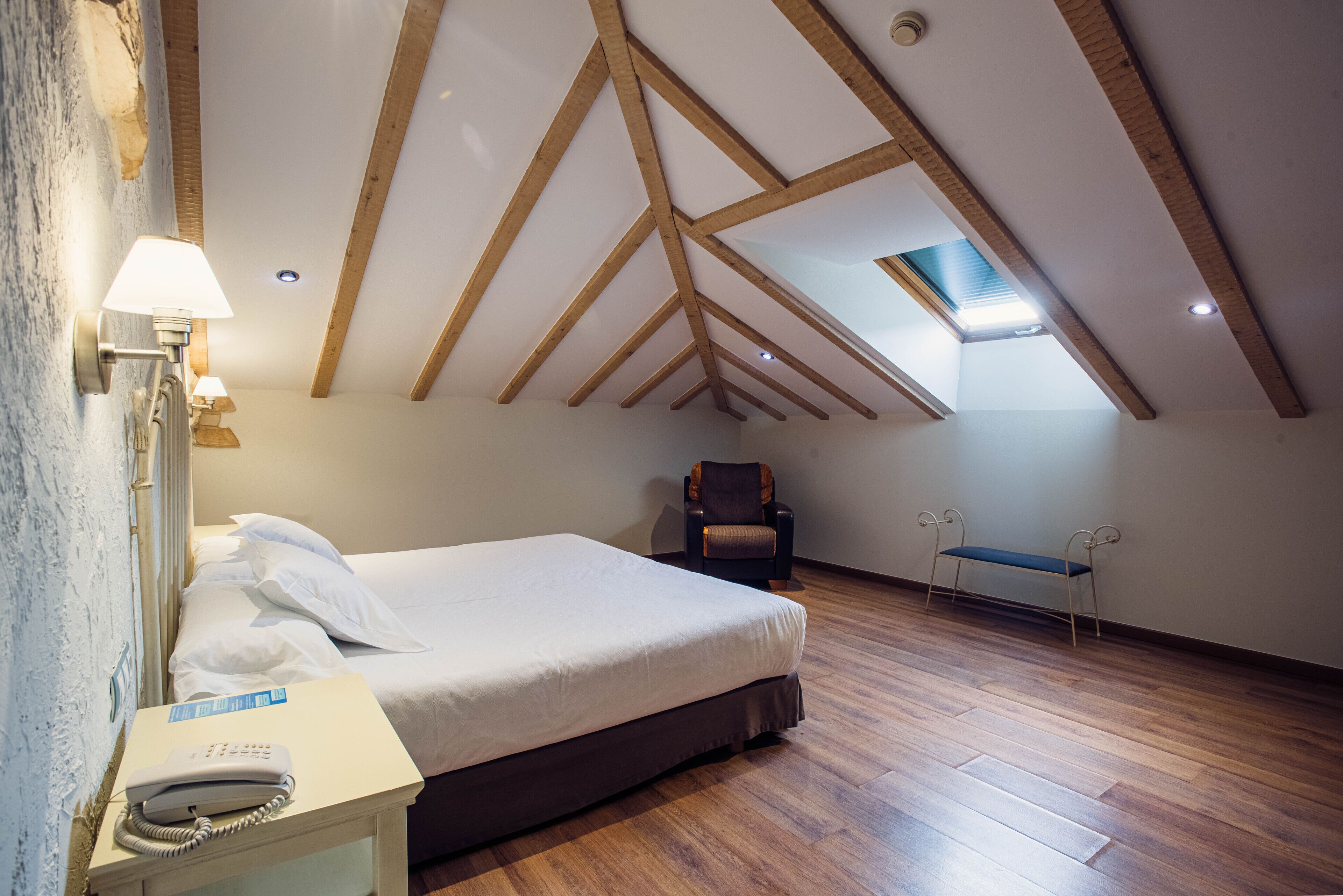 A bedroom with a wooden ceiling, a bed, a chair, and a bench.