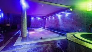 Un espacio de spa con un amplio jacuzzi, una pared de piedra y suelo de baldosas.