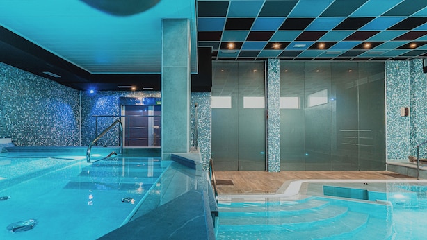 Una piscina interior moderna con agua cristalina, un muro de vidrio y una pared de azulejos con un diseño de mosaico azul.