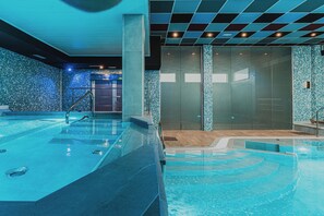 Una piscina interior moderna con agua cristalina, un muro de vidrio y una pared de azulejos con un diseño de mosaico azul.