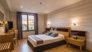 A hotel room with a bed, bedside tables, a desk, a chair, and a TV.
