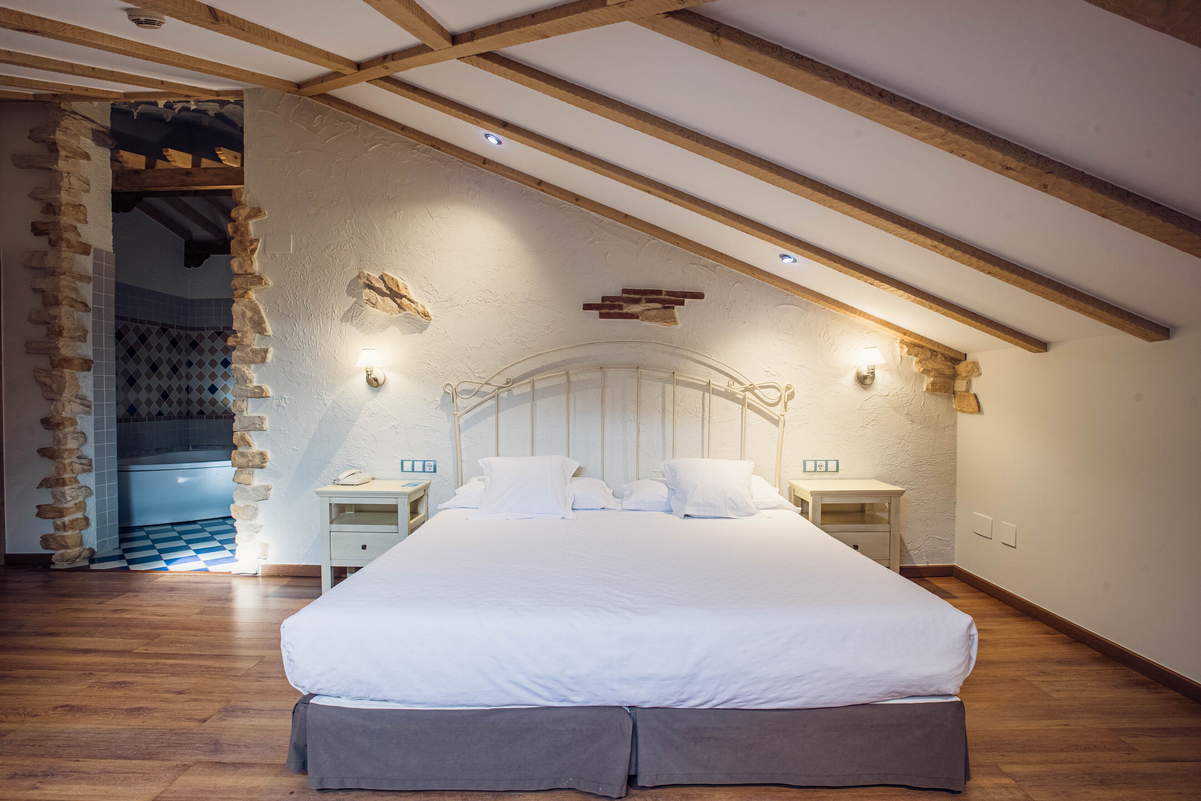 Ein Schlafzimmer mit einem großen Bett, Holzbalken, Steinwänden und einem Schachbrettmuster-Boden.
