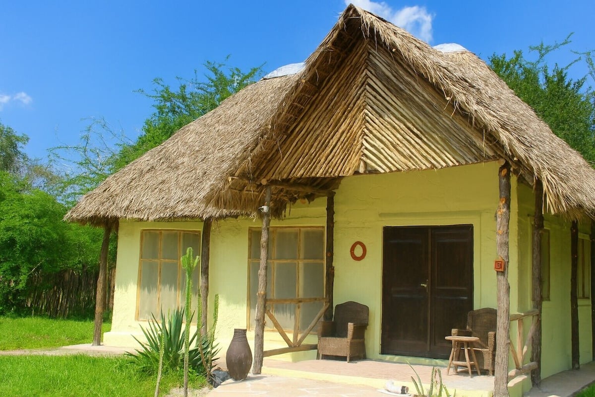 A thatched-roof building with a porch, large windows, and a door.
