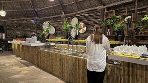 A buffet setup with a central serving counter, surrounded by a bamboo wall and thatched ceiling. - Africa Safari Selous (Selous Game Reserve)