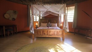 A wooden four-poster bed with a canopy, a woven rug, and a wooden table with a chair. - Africa Safari Selous (Selous Game Reserve)
