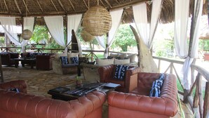 A covered outdoor seating area with leather sofas, a coffee table, and hanging wicker lamps. - Africa Safari Selous (Selous Game Reserve)