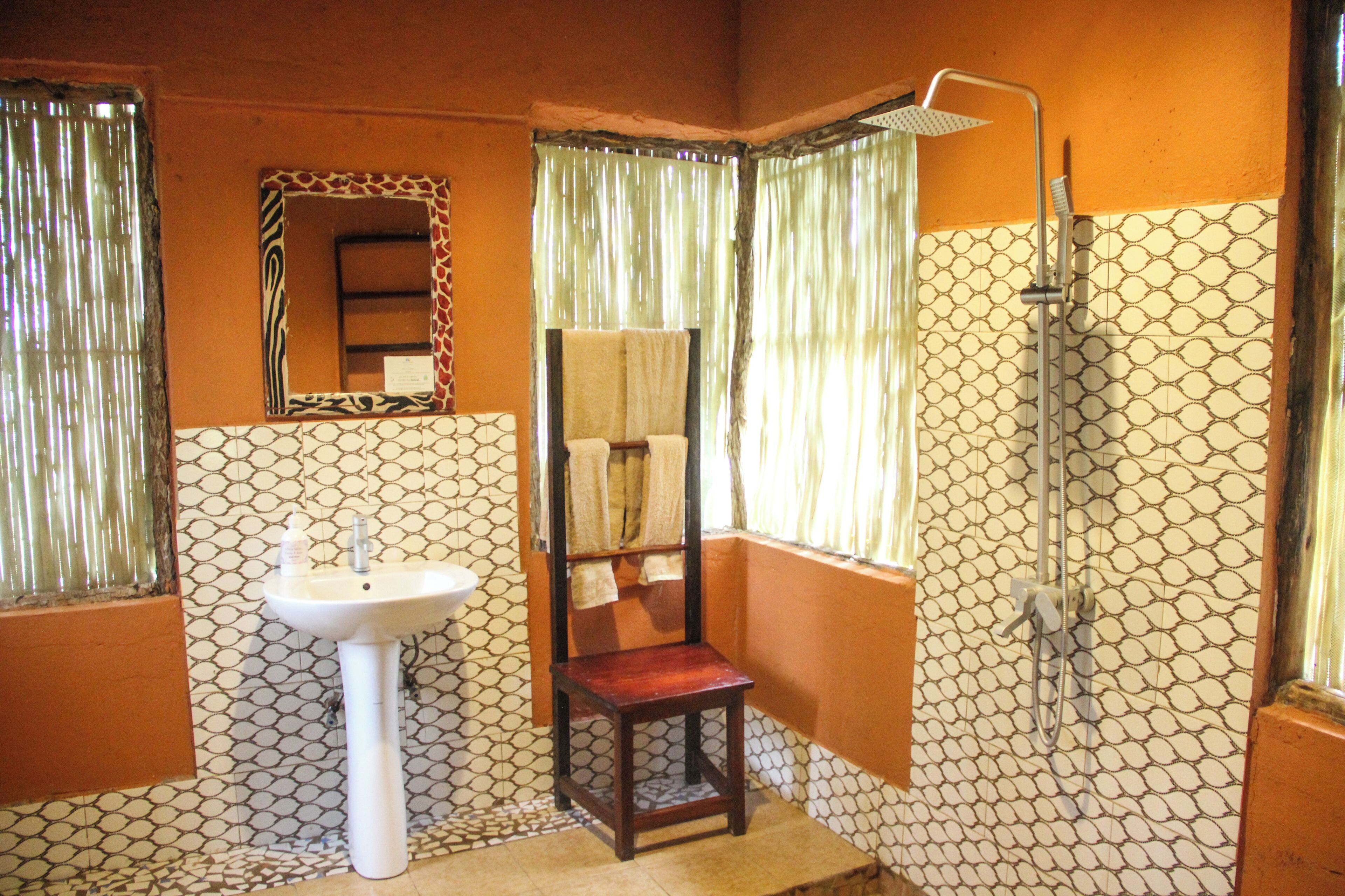 Un baño con lavamanos blanco, una silla de madera, una ducha y paredes con diseño.