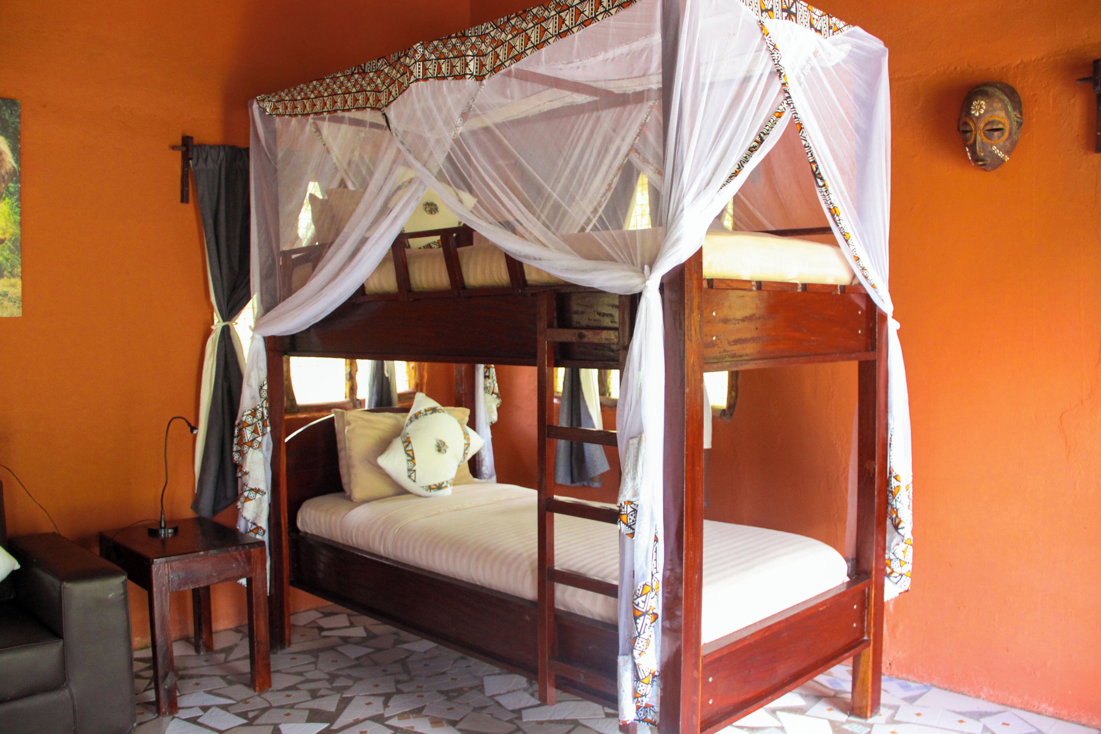 A four-poster bed with a canopy, a small wooden table, and a wall-mounted mask.