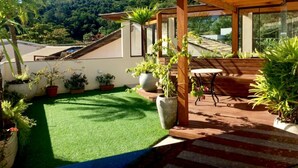 A covered patio area with a wooden pergola, a small table, and several potted plants. - Pousada Pedra Rosa (Florianópolis)