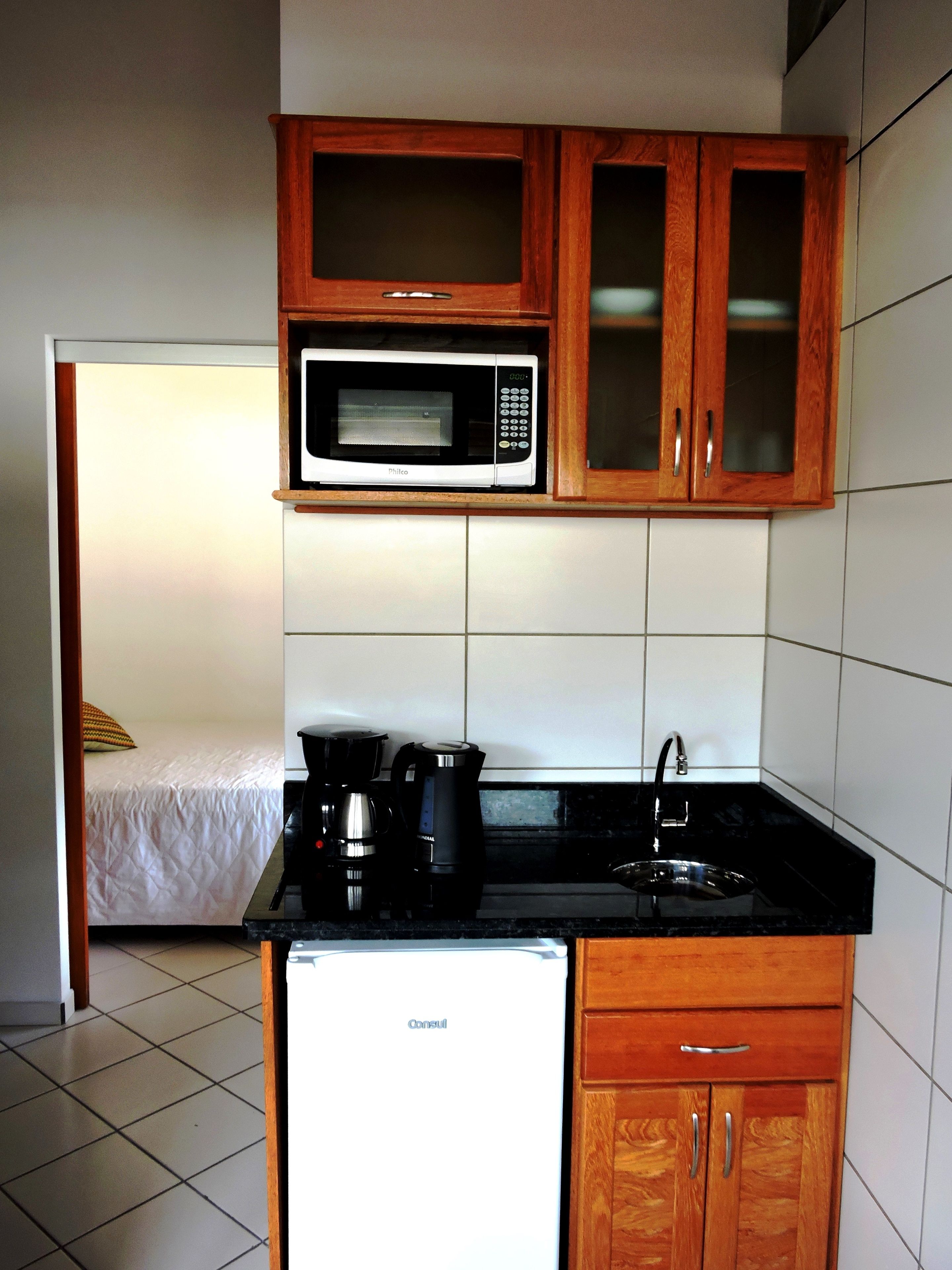 Una kitchenette compacta con microondas, cafetera y refrigerador.