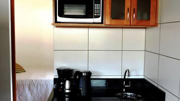 Una kitchenette compacta con microondas, cafetera y refrigerador.