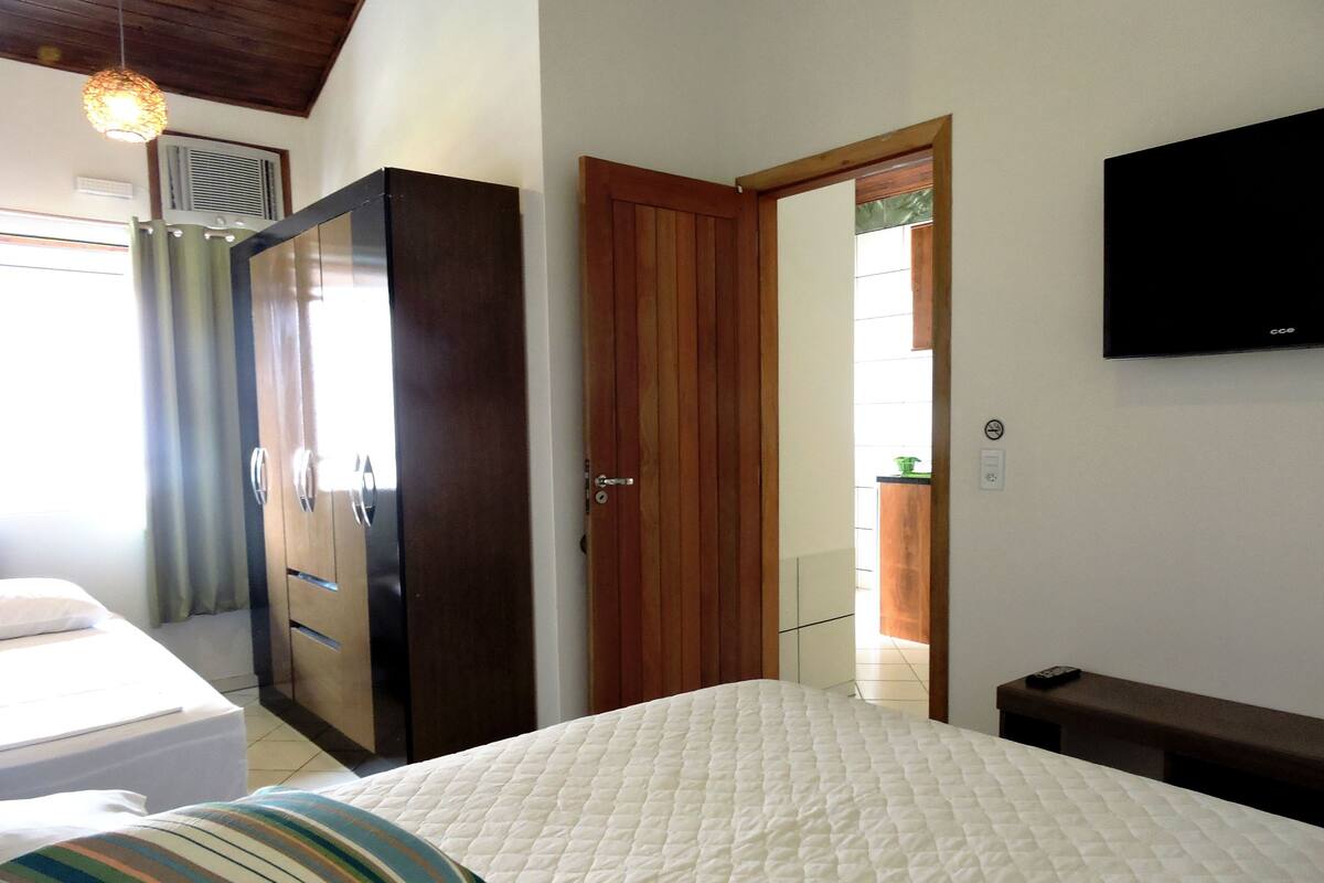 Une chambre à coucher comprenant un lit, une armoire, un téléviseur et une porte donnant sur une salle de bain.