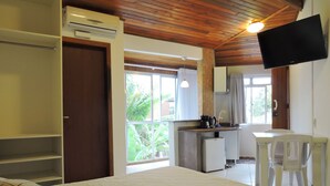 A bedroom with a bed, a wardrobe, a kitchenette, a desk, and a TV. - Pousada Pedra Rosa (Florianópolis)