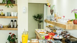 A buffet setup with various food items and beverages, including fruits, pastries, and a juice dispenser. - Pousada Pedra Rosa (Florianópolis)