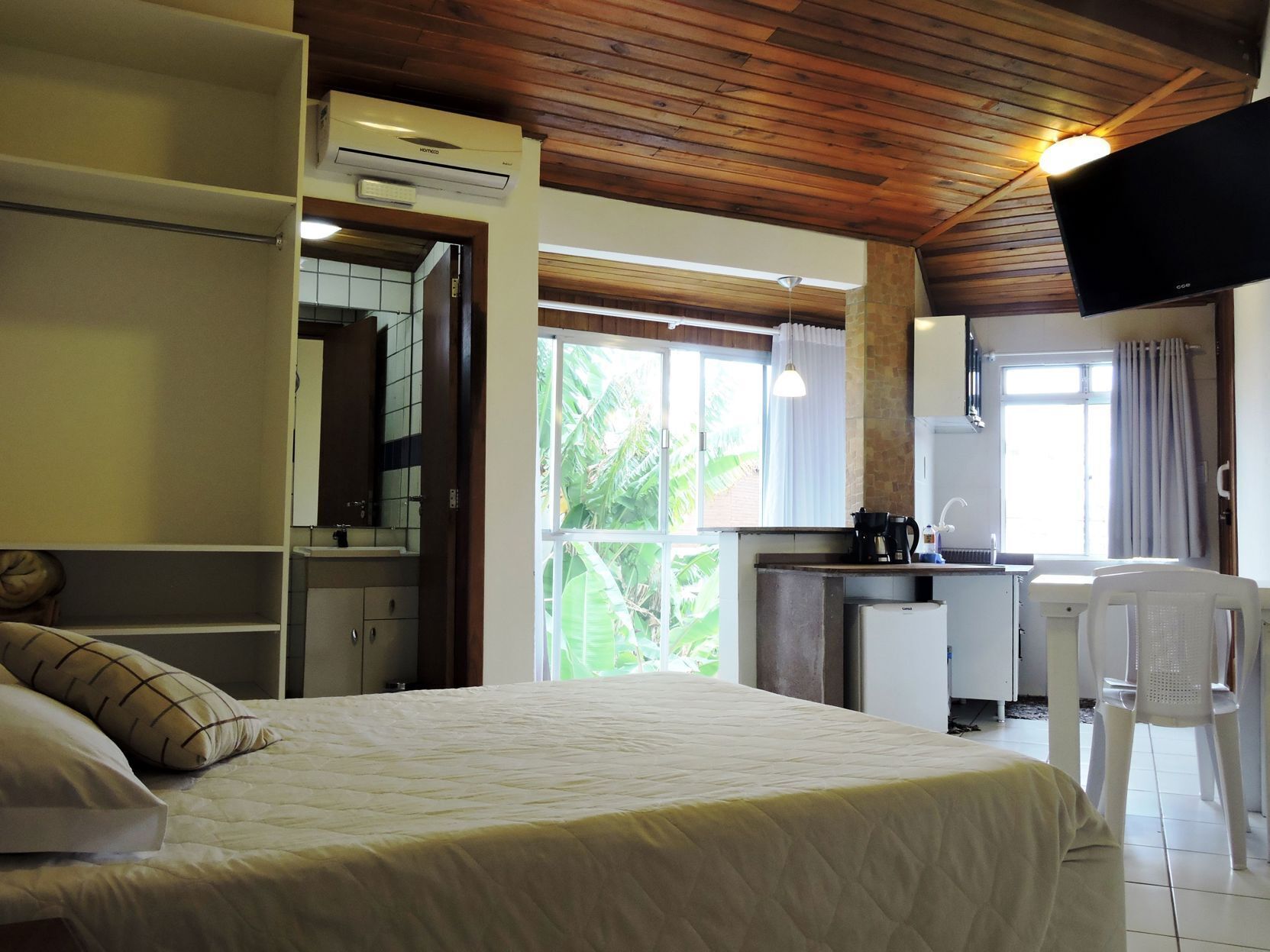 Un dormitorio con cama, escritorio, silla, televisión y ventana con vistas al verdor.