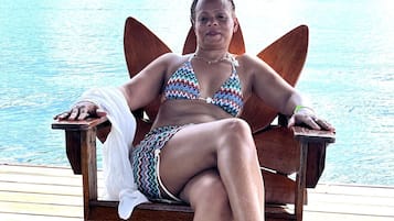 Una persona sentada en una silla de madera con vista a un cuerpo de agua y edificios al fondo.