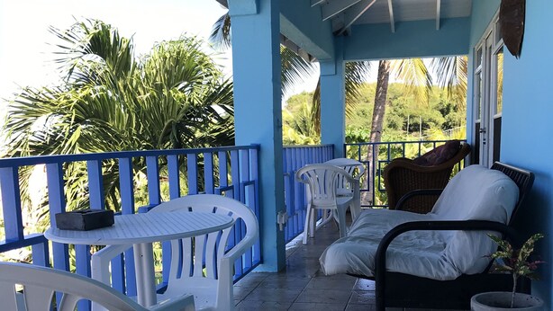 A covered outdoor seating area with blue railings, white plastic chairs, a table, and a black sofa. - Ellen Bay Cottages (Seatons Village)