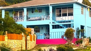 A two-story building with balconies, a stone wall, and a pink ground floor. - Ellen Bay Cottages (Seatons Village)