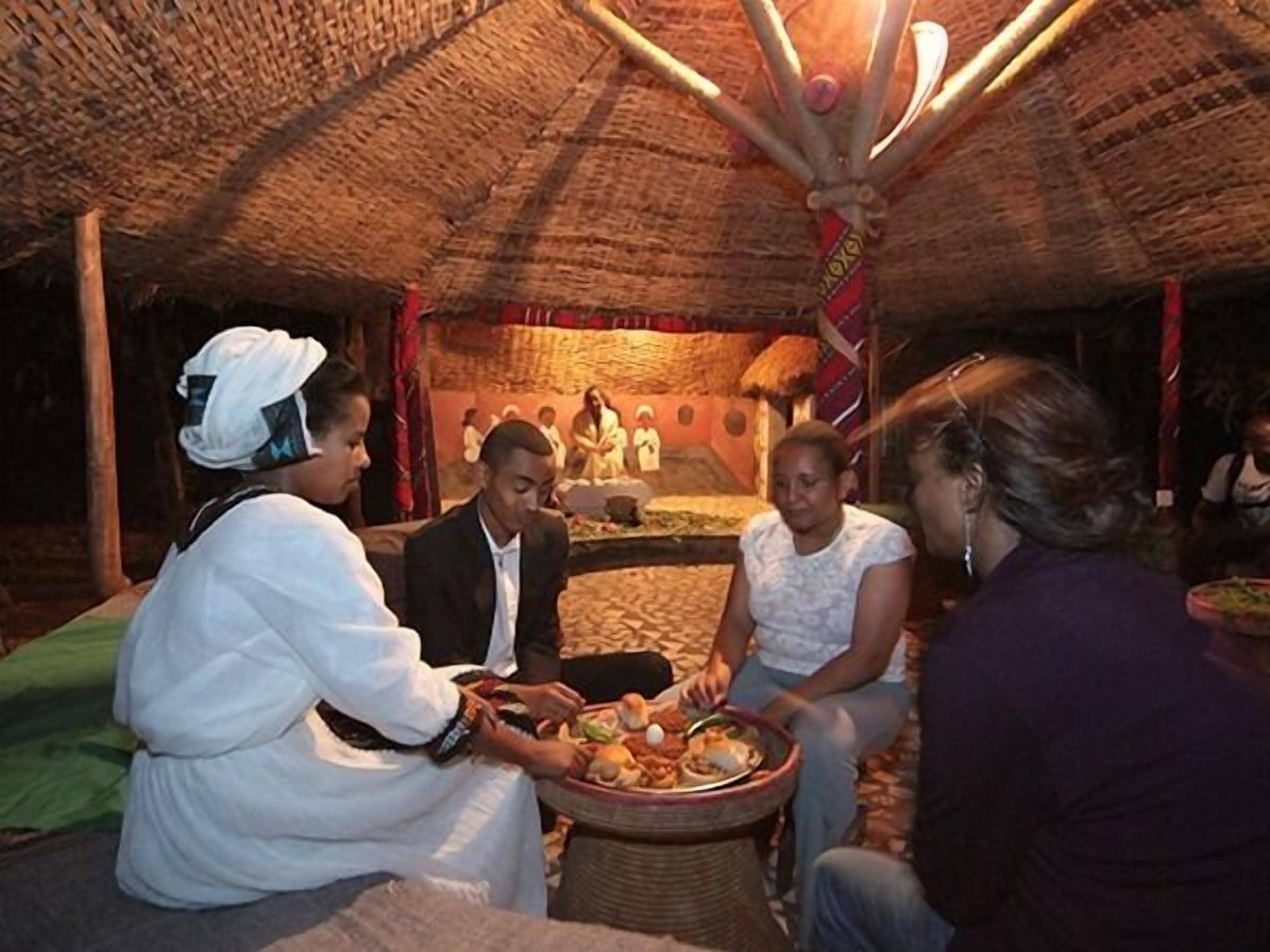 A traditional setting with a thatched roof, a central seating area, and a person serving food.