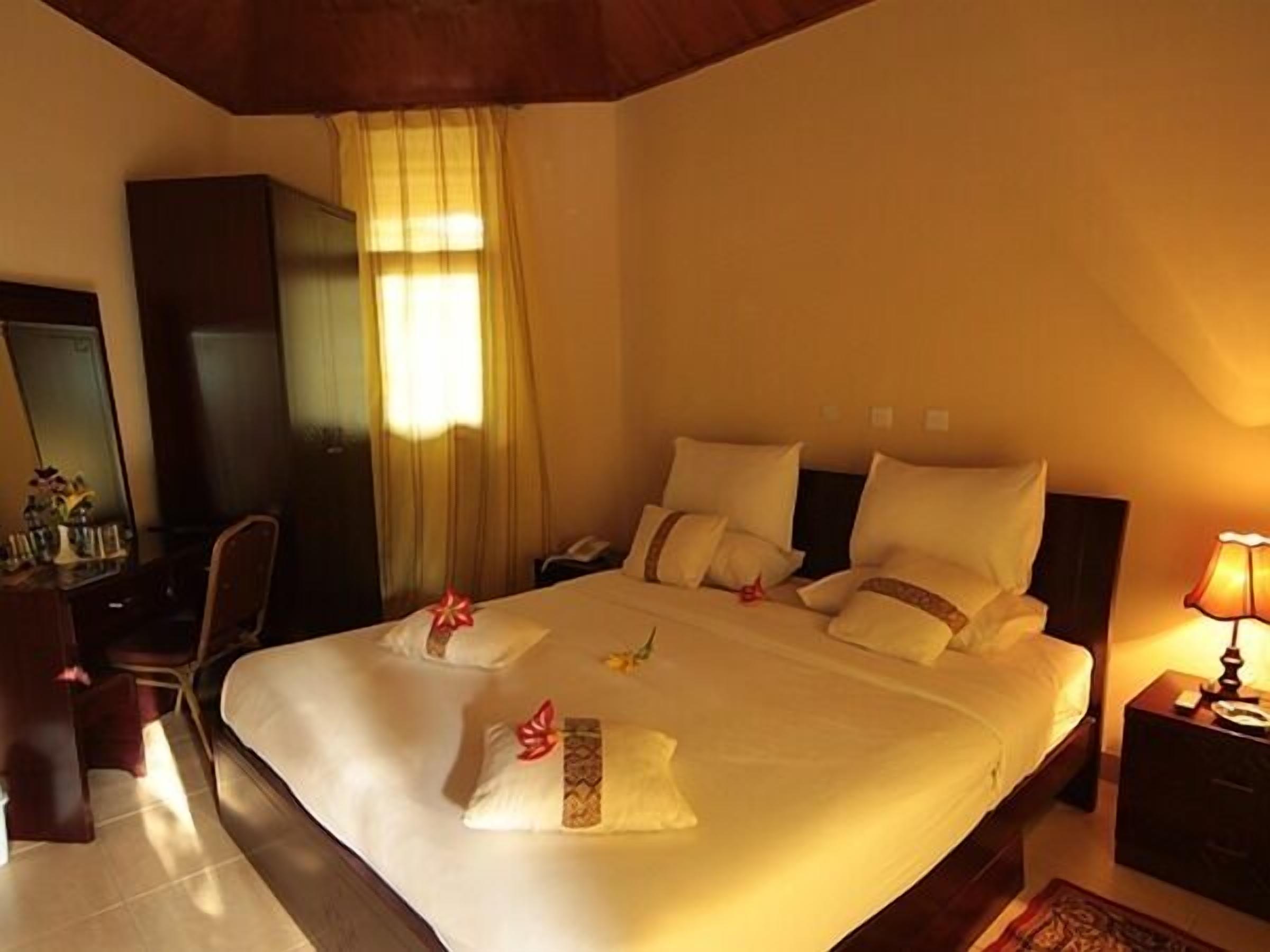 A hotel room with a bed, bedside tables, a desk, and a mirror.