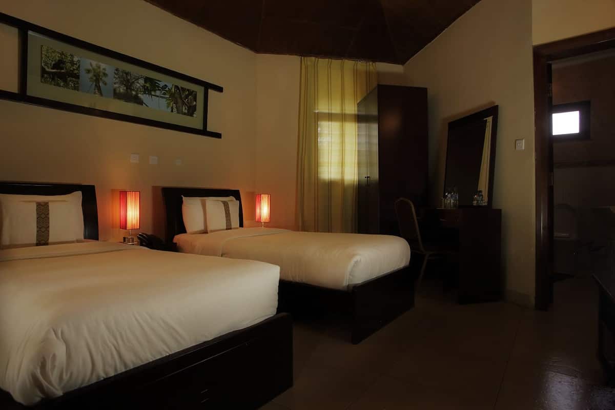 Ein Hotelzimmer mit zwei Betten, einem Schreibtisch, einem Stuhl, einem Spiegel und einem gerahmten Bild an der Wand.
