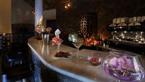 Una zona de bar con mostrador de mármol, botellas de vino, copas y una estantería para vinos al fondo.