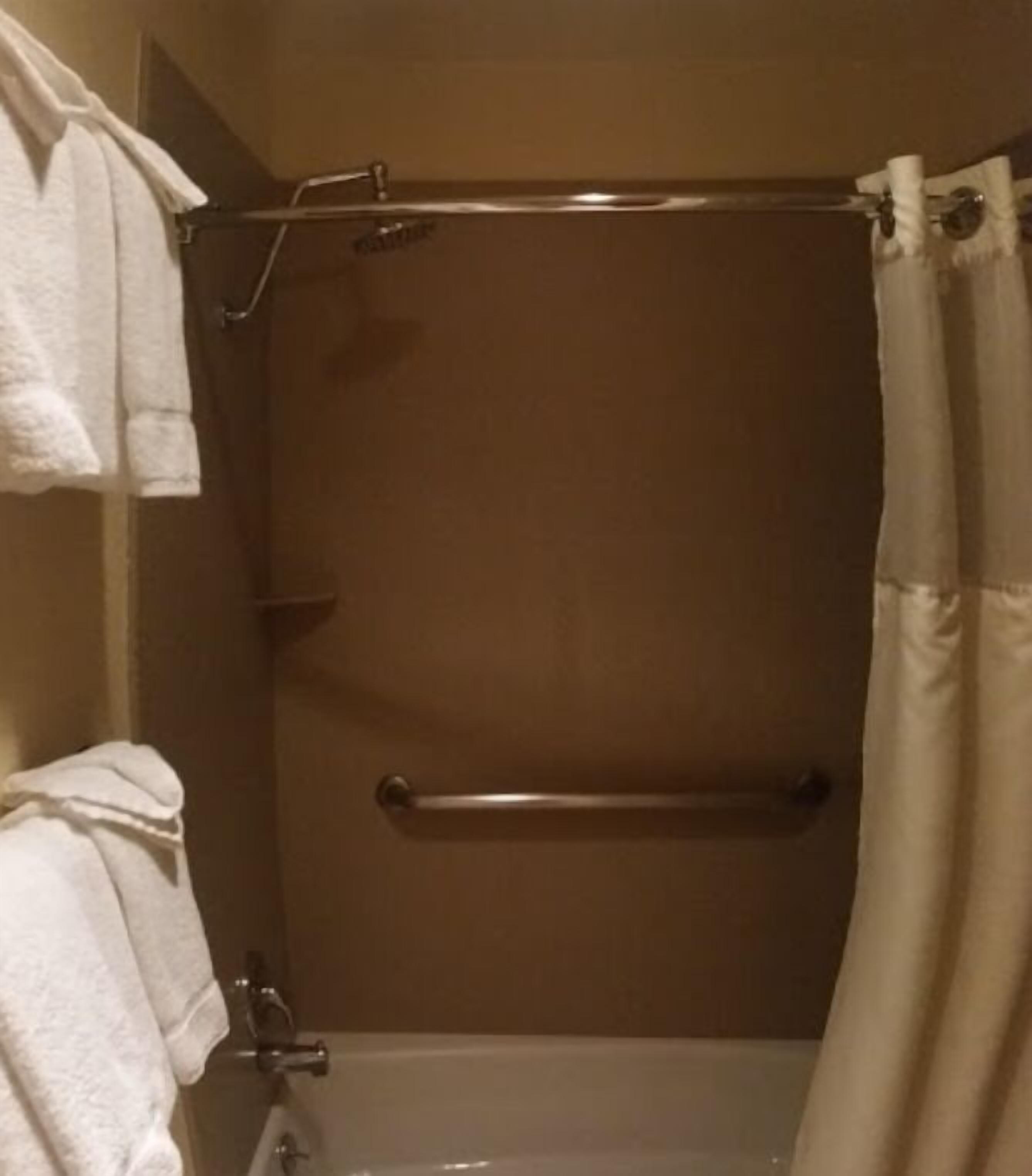A bathroom with a bathtub, a shower curtain, and a grab bar.