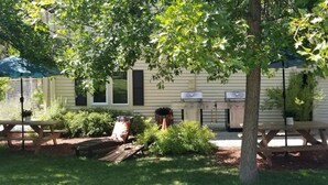 A backyard with a grill, picnic tables, and a tree providing shade.