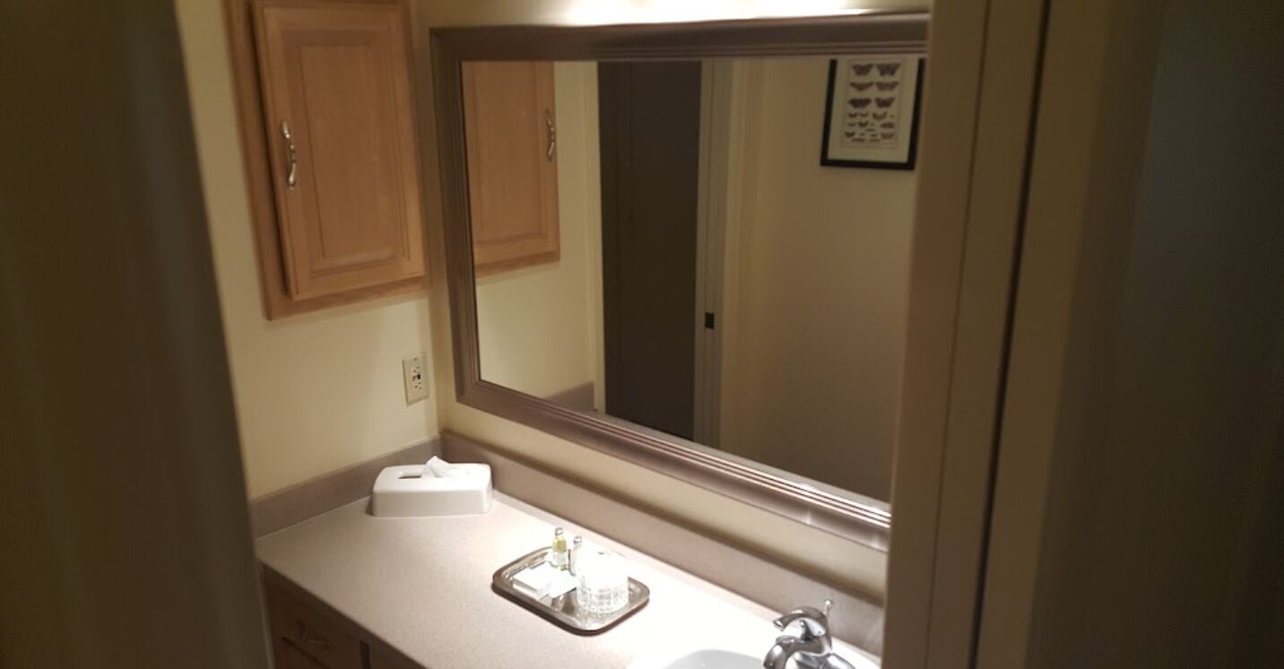 A bathroom with a large mirror, a sink, and a towel dispenser.