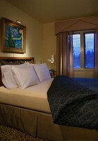 A hotel room with a large bed, a painting on the wall, and a window with curtains.
