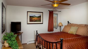 Un dormitorio con cama, televisión, ventilador de techo, ventana con cortinas e imagen enmarcada en la pared.