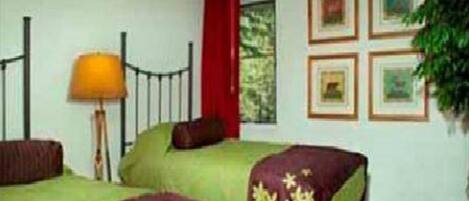 A room with two beds, a ceiling fan, a window with red curtains, and framed pictures on the wall.