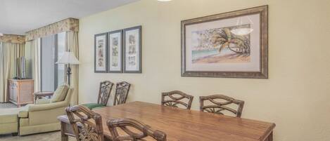 A dining area with a wooden table and chairs, a chandelier, and framed artwork on the wall.