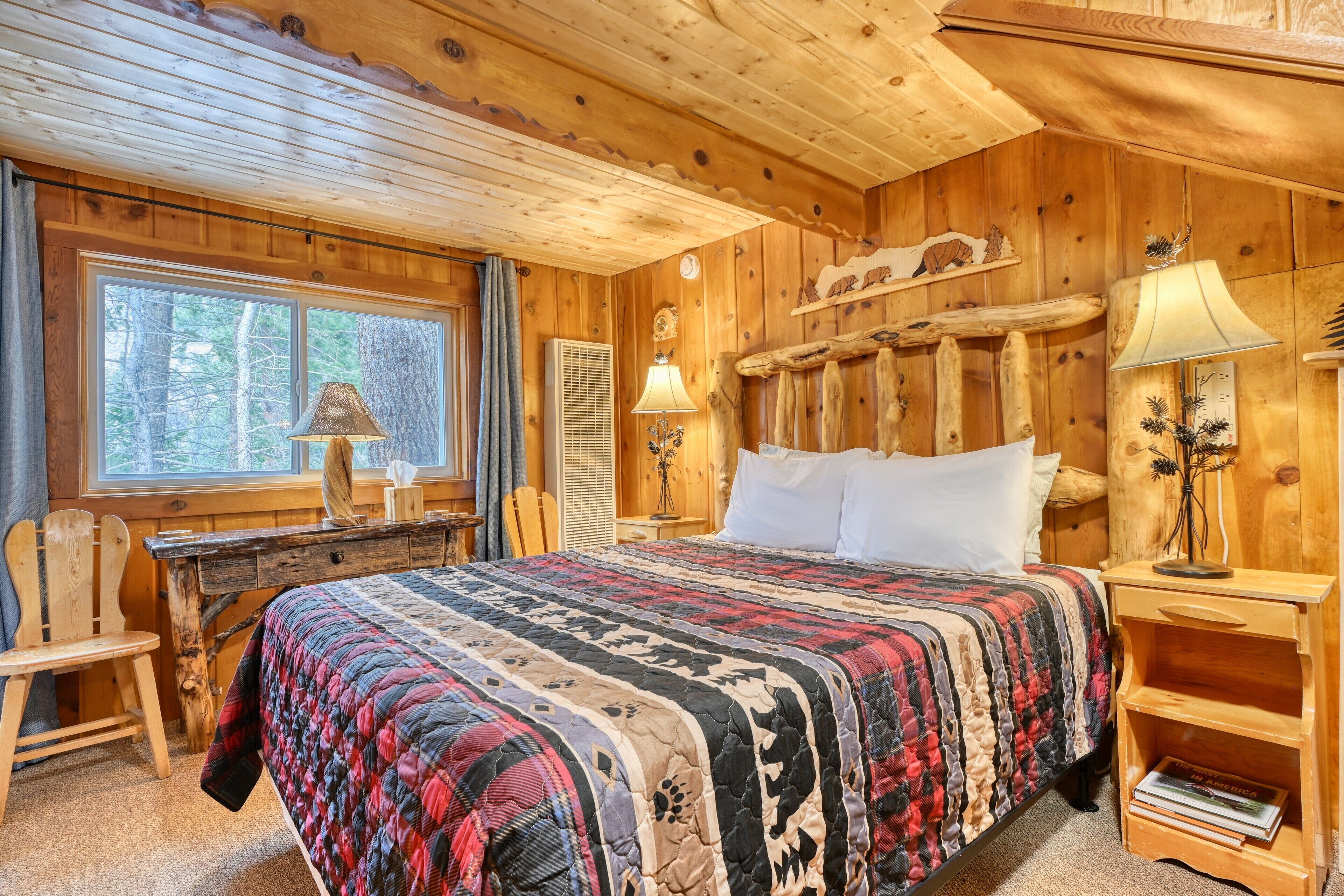 A wooden cabin bedroom with a large bed, a desk, and a chair.