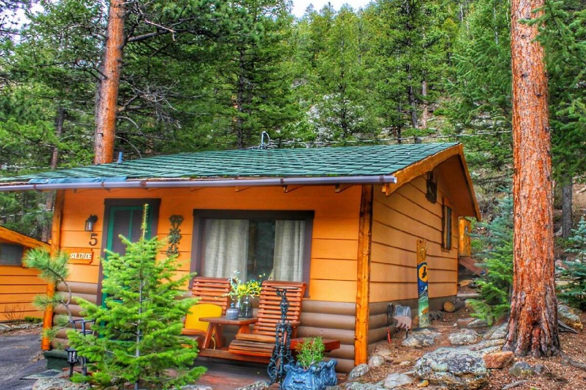 A log cabin with a green roof, a porch with wooden chairs, and a small table.