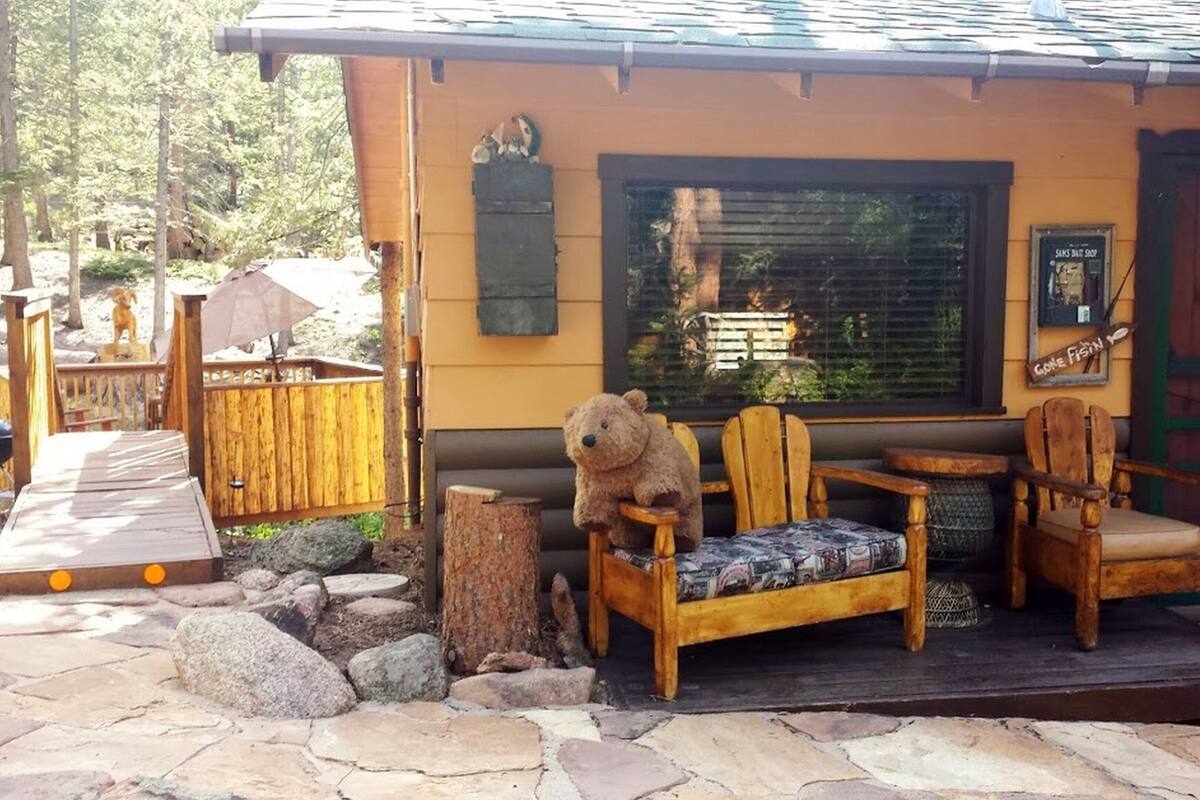 A wooden cabin with a porch, a bear sculpture, and a sign that reads "Gone Fish."